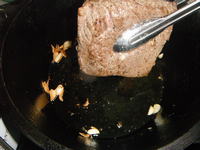 焼き目がつけられた牛もも肉をトングを使ってダッチオーブンから取り出そうとしています。