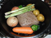 ダッチオーブンの中で牛もも肉のまわりにジャガイモ、にんじん、ピーマン玉ねぎ、アスパラが丸ごと並べられています。