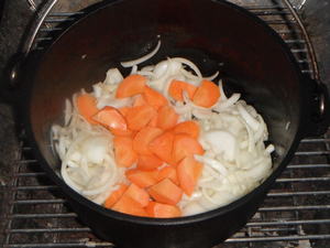 ダッチオーブンの中で炒められた玉ねぎの上にニンジンが追加されています。