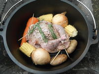 ダッチオーブンの中で丸鶏の周りに野菜が並べられています。